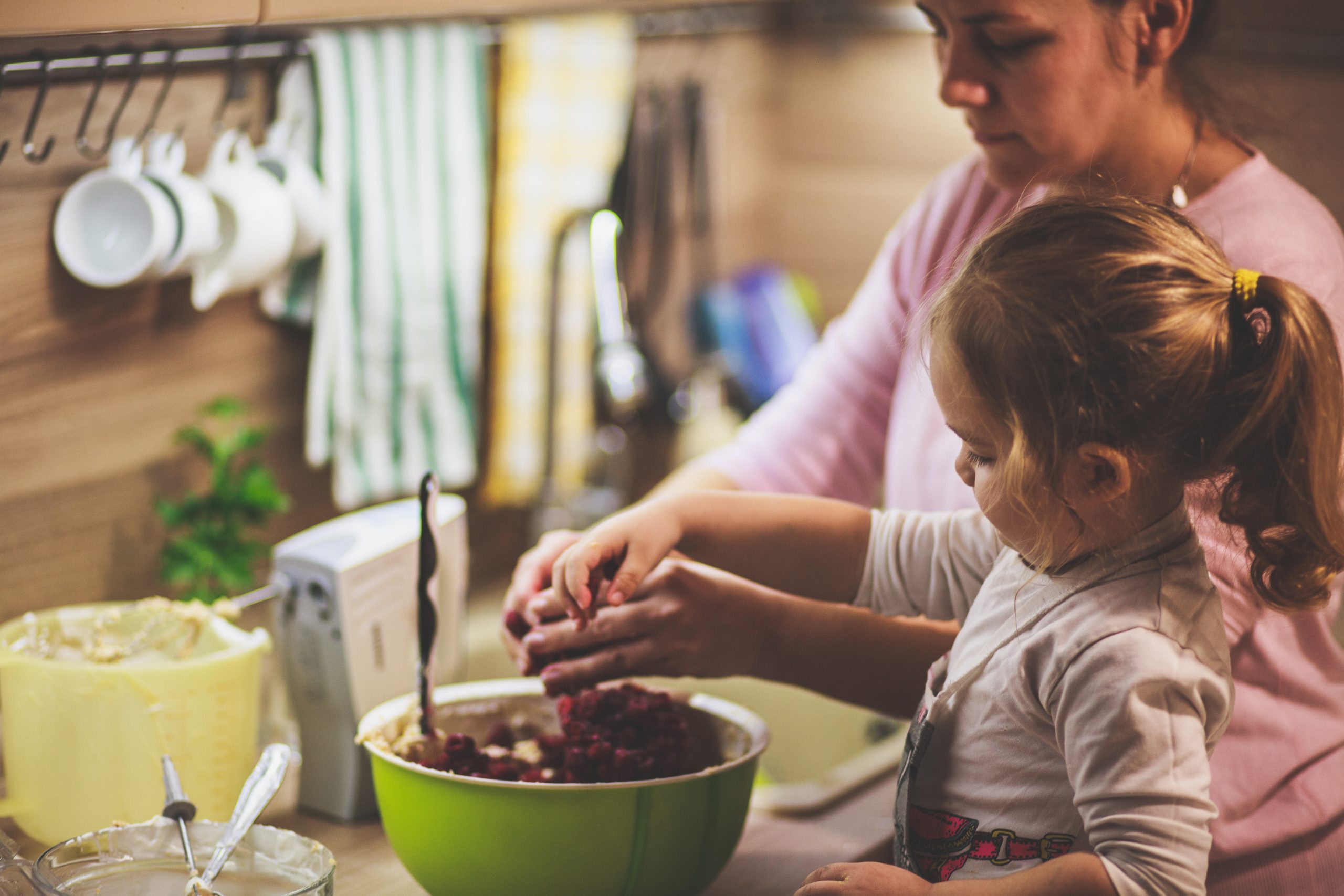 Little girl mixing cherries in the cake batter with her mother